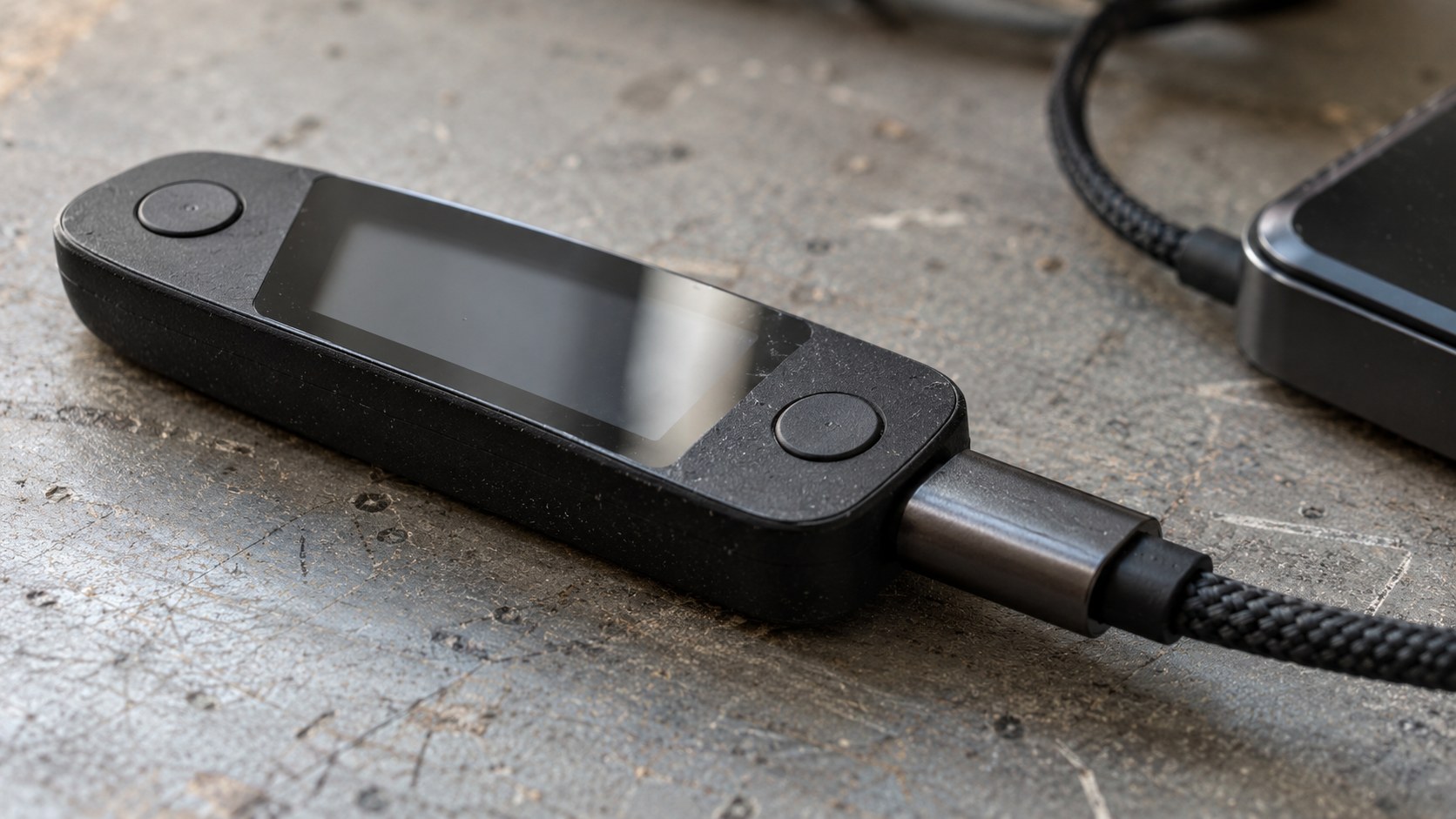 Close view of an unbranded hardware wallet with two confirmation buttons and a braided cable connected to a test.